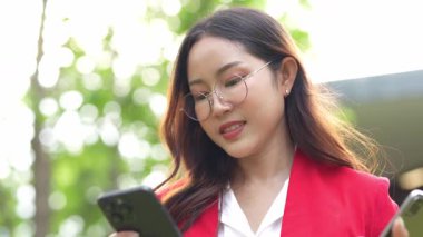 Asyalı iş kadını cep telefonu kullanıyor, akıllı telefonuyla modern ofis dışındaki iş arkadaşlarıyla mesajlaşıyor ve sohbet ediyor..