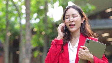 Asyalı iş kadını cep telefonu kullanıyor, akıllı telefonuyla modern ofis dışındaki iş arkadaşlarıyla mesajlaşıyor ve sohbet ediyor..