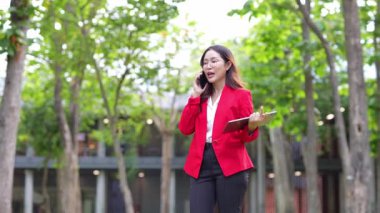 Asyalı iş kadını cep telefonu kullanıyor, akıllı telefonuyla modern ofis dışındaki iş arkadaşlarıyla mesajlaşıyor ve sohbet ediyor..