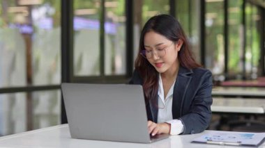 Masada çalışan Asyalı iş kadını dizüstü bilgisayar ve not defteri kullanarak müşteri ya da ofis binasıyla konuşuyor, yavaş çekim görüntüleri