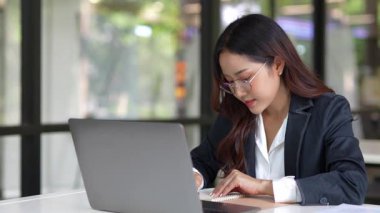 Masada çalışan Asyalı iş kadını dizüstü bilgisayar ve not defteri kullanarak müşteri ya da ofis binasıyla konuşuyor, yavaş çekim görüntüleri