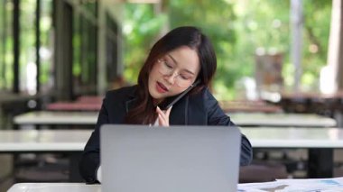 Masada çalışan Asyalı iş kadını dizüstü bilgisayar ve not defteri kullanarak müşteri ya da ofis binasıyla konuşuyor, yavaş çekim görüntüleri