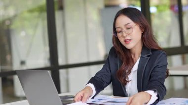Masada çalışan Asyalı iş kadını dizüstü bilgisayar ve not defteri kullanarak müşteri ya da ofis binasıyla konuşuyor, yavaş çekim görüntüleri