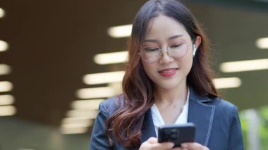 Asyalı iş kadını cep telefonu kullanıyor, akıllı telefonuyla modern ofis dışındaki iş arkadaşlarıyla mesajlaşıyor ve sohbet ediyor..