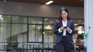 Asyalı iş kadını cep telefonu kullanıyor, akıllı telefonuyla modern ofis dışındaki iş arkadaşlarıyla mesajlaşıyor ve sohbet ediyor..