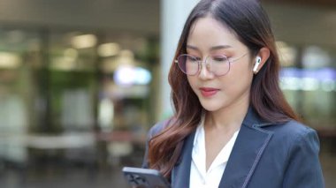 Asyalı iş kadını cep telefonu kullanıyor, akıllı telefonuyla modern ofis dışındaki iş arkadaşlarıyla mesajlaşıyor ve sohbet ediyor..