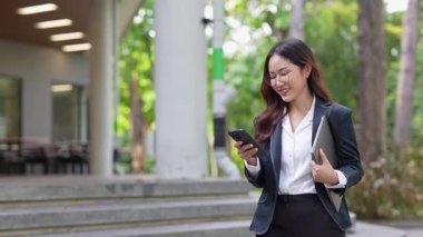 Asyalı iş kadını cep telefonu kullanıyor, akıllı telefonuyla modern ofis dışındaki iş arkadaşlarıyla mesajlaşıyor ve sohbet ediyor..