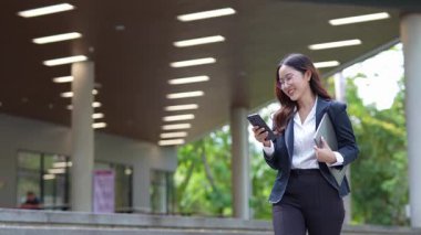 Asyalı iş kadını cep telefonu kullanıyor, akıllı telefonuyla modern ofis dışındaki iş arkadaşlarıyla mesajlaşıyor ve sohbet ediyor..