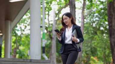 Asyalı iş kadını cep telefonu kullanıyor, akıllı telefonuyla modern ofis dışındaki iş arkadaşlarıyla mesajlaşıyor ve sohbet ediyor..