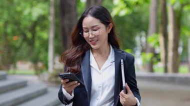 Asyalı iş kadını cep telefonu kullanıyor, akıllı telefonuyla modern ofis dışındaki iş arkadaşlarıyla mesajlaşıyor ve sohbet ediyor..