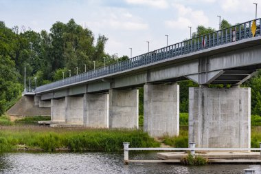 Yaz bulutlu bir günde yeşil ağaçların arasında nehir üzerinde bir köprü. Nehir.