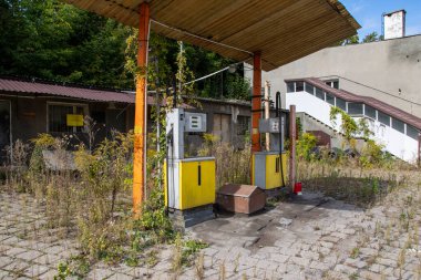 Old rusty gas station and dispensers abandoned and overgrown with vegetation on a sunny day. Summer.