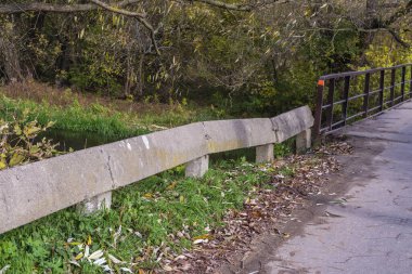 A concrete railing by a deserted and neglected road on a gloomy autumn day.