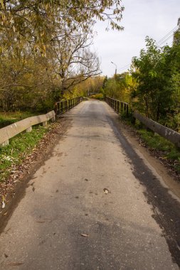 A concrete railing by a deserted and neglected road on a gloomy autumn day.