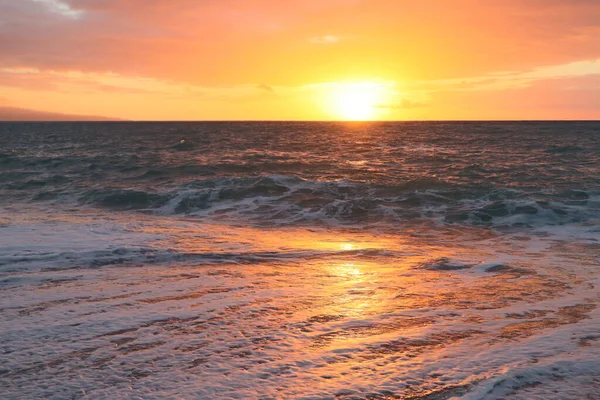 Sunset over a stormy sea on the sea coast of Italy. The orange sun on the horizon reflects on the surface of the water. Scenic seascape waves and sea foam on the beach in the rays of the orange sun at sunset
