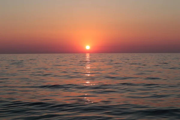 Sunset over the pink sea on a summer evening. Seascape sky and sea in the rays of the setting sun, orange-pink sky blue by the sea, the sun on the horizon is reflected on the surface of calm water