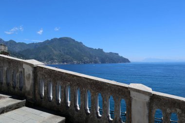Güneşli bir yaz gününde, dağları ve denizi panoramik manzaralı kayalık bir sahilde demiryolu merdiveni olan Atrani, İtalya