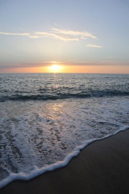 Kumsalda gün batımı, ufukta güneş, bulutlarda deniz köpüğü ve batan güneşin ışınlarında ıslak kum.,