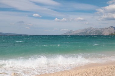 Fırtına sırasında resim gibi plaj, kayalarda beyaz köpük ve gökyüzünde beyaz bulutlar, deniz manzarası.