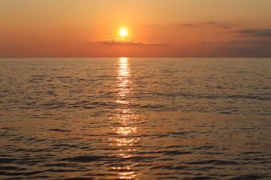 Gün batımında deniz manzarası, batan güneşin ışınlarında bulutlar ve deniz. 