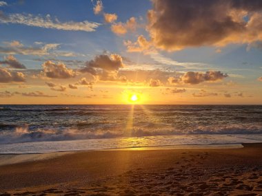 Kumsalda gün batımı, deniz köpüğü ve batan güneşin ışınlarıyla deniz kıyısında ıslak kum..