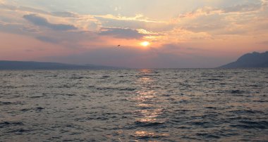 Sahilde gün batımında deniz manzaralı bulutlar ve ufukta güneş, Brela, Hırvatistan