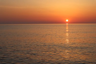 Suyun üzerinde gün batımı, ufukta parlak turuncu güneş, denizin yüzeyine yansıyan güneş ışınları. Tyrhenian Denizi, İtalya