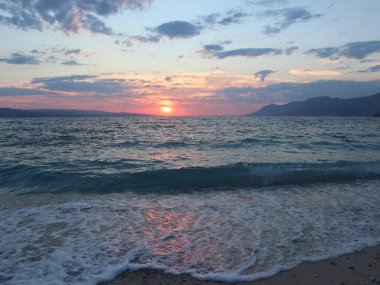 Deniz üzerinde gün batımında parlak güneş deniz köpüğüne, kumlara ve sahildeki ıslak taşlara yansıyor..