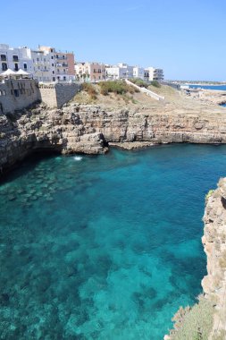 Uçurumun tepesindeki beyaz evleri ve turkuvaz suyu olan denizi, şeffaf suyun altındaki kayaları, Polignano a Mare, İtalya 'daki plajları görebilirsiniz.