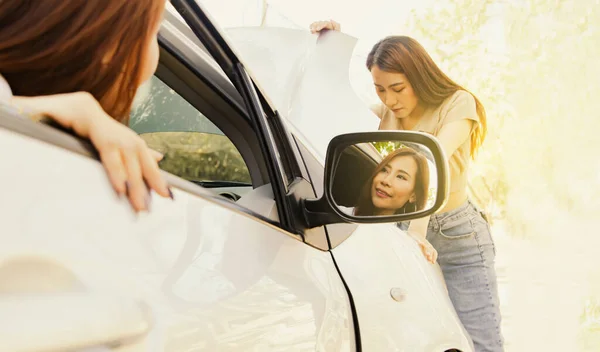 Female friend stood to inspect the damaged engine initially calmly and consciously  the car was parked side of the road while traveling with friend sitting in the car waiting for help without worry.