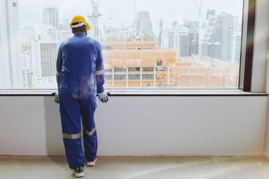 Asyalı bir erkek işçi şehrin yüksek bir inşaat sahasında çalışıyor camdan dışarı bakıyor ve olumlu ve ilham verici başarılar düşünüyor..