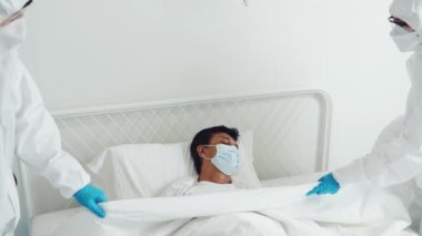 Üşütmüş yaşlı hastalarla ilgilenen PPE giysileri giyen tıbbi ekip, karantina sırasında akciğerlerindeki enfeksiyondan ölen hastanın vücudunu örtbas ediyor..