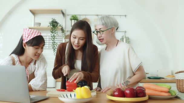 アジアの家族 お母さんと2人の幸せな娘は幸せと一緒にキッチンで一緒に料理を栄養 興味深いことにオンラインメディアによると調理方法を見て — ストック動画