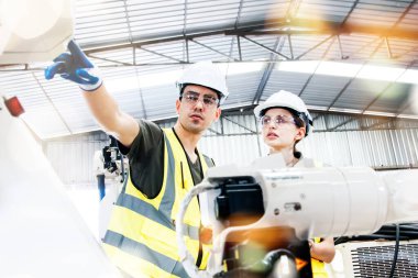 Architect team. Male and female electronic technicians operating electric welding robot arms in factory warehouse. Automated testing by industrial circuit experts consults and guides safe operation.