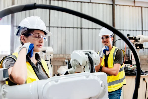 Female electrician working robotic arm taking break, calm and concentrating while male architect friends stand and watch with ease in industrial factory : Electrician engineer working team.