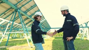 Erkek ve kadın elektrik mühendislerinden oluşan bir ekip, bir elektrik santralinin güneş paneli kurulum alanını kontrol eder, koruyucu bakım ve el sıkışma görevini birlikte tamamlar..