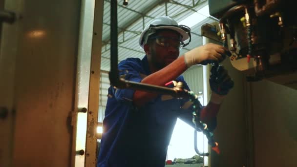 アフリカ系アメリカ人男性技術者は 冷却管 自律鋼カッター ドリルを検査し 効率的な運転のための安全性を確保します — ストック動画