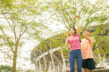 Kol kaslarını güçlendirmek ve dengelemek için dambıllarla spor yapan Asyalı genç çift: etkinlik eğlencesi egzersizi sabah sağlıklı yaşam tarzı.