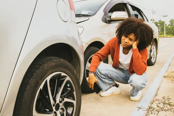 stock image African American woman with shocked expression drove recklessly crashing into the rear of the car and damaging the front Sitting distraught looking at the damage to her car there was no car insurance.