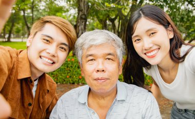 Üç çocuklu Asyalı bir ailenin portresi, mutlu bir gülümseme sergiliyor parkta sağlıklı babayla fotoğraf çekiyor: Emekli yaşlı konsepti için sağlık sigortası.