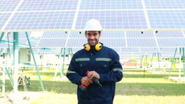 Portre yakışıklı erkek elektrik mühendisi güneş panelini koruyor. Saha çalışması için elektrikli matkap tutuyor. Temiz güneş enerjili elektrik santrali kameraya bakıyor ve gülümsüyor..