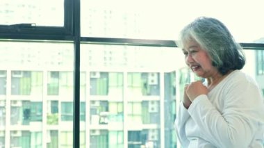 Asian elderly woman sitting by window looking at laptop following online exercise advice Stretch your arms and switch sides inside the condominium for mental health to relax.