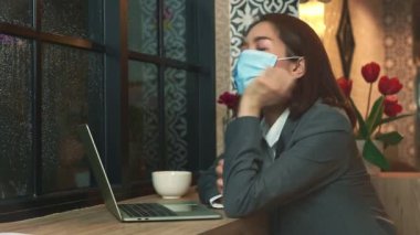 Ofis işini bitirdikten sonra Asyalı iş kadını kafeteryada kahve içerken maske takmış, yağmurun dinmesini bekliyor..