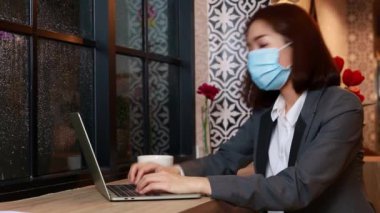 Ofis işini bitirdikten sonra Asyalı iş kadını kafeteryada kahve içerken maske takmış, yağmurun dinmesini bekliyor..
