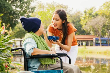Asyalı bir aile, müteşekkir bir kız çocuğu hasta ve felçli bir anneye bakıyor, vücudunu iyileştirmek ve onu sağlıklı tutmak için yemeğini besliyor: