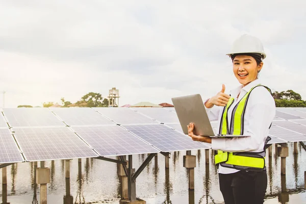 Professional asian female electrical engineer in helmet working in field working solar panel installation site in suburban area positive result thumbs up on tablet online to connect with communication