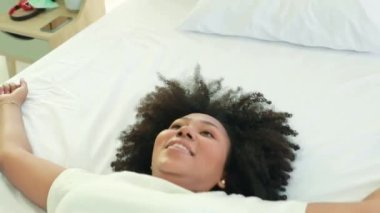 Top view portrait of african american woman lying in bed at home in her bedroom having fun in bed having fun before going to bed Looking at the camera and laughing, waving hello.