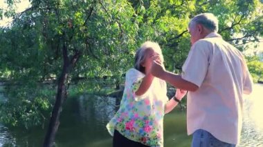 Healthy and happy Asian senior couple relaxes with lively dancing and singing in a park by a shady pond on weekends.