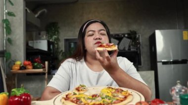 Obese Asian woman sits and eats her favorite glutton snack food pizza with great relish, she eats too much causing her throat to choke : Fat woman eating pizza unhealthy  overeating.