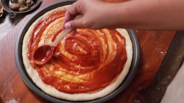 Hands female chef kitchen making homemade pizza garnishing the surface marinated dough smearing delicious red tomato sauce on the surface prepare pizza toppings and cheese before going in the oven.